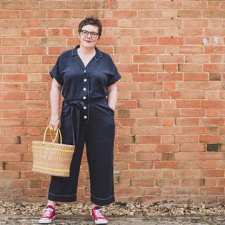 Female wearing Cressida Jumpsuit Sewing Pattern in navy fabric standing in front of a brick wall