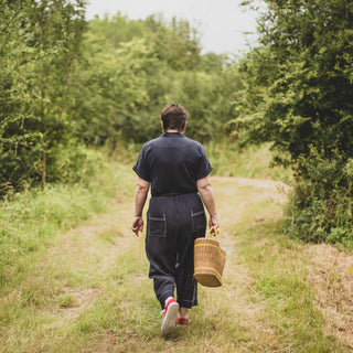Female in the woods walking away from the camera wearing a Cressida Jumpsuit sewing pattern in navy fabric